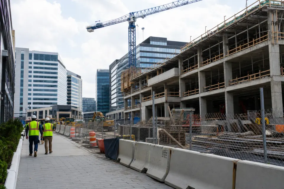 A concrete mixed-use building under construction beside Tysons office towers