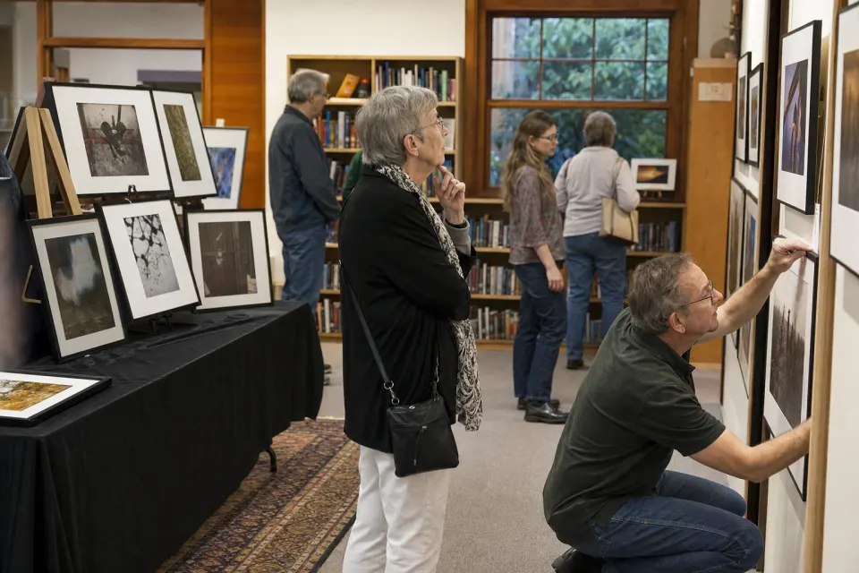 Visitors viewing framed photographs in a community library exhibition room