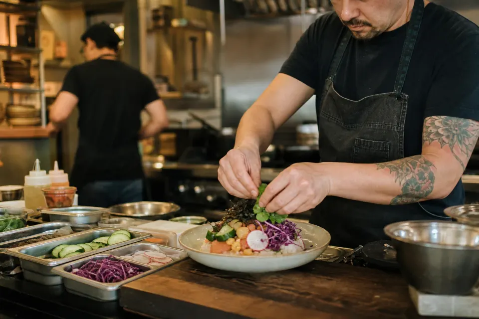 A cook plating vegetables and grains in a busy independent restaurant kitchen